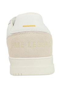 Baskets blanches avec un talon en daim beige, des coutures jaunes proéminentes et une marque en relief "PME LEGEND" près du talon. Semelle en caoutchouc plate.