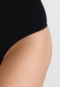 Culotte en coton noire taille haute avec une texture lisse et une taille élastique, montrant un gros plan du tissu et des détails de conception.
