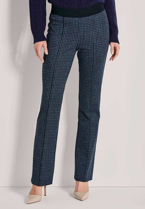 Marineblau gemusterte Hose mit einem taillierten Bund. Vertikale Streifen in Hellblau und Grün auf einem strukturierten Stoff. Kombiniert mit beigen Absatzschuhen.