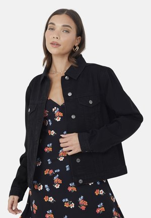 Veste en denim noir avec col, fermeture à boutons et deux poches poitrine. Portée sur une robe à fleurs avec des accents rouges et bleus.
