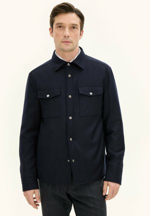 Navy blue shirt jacket featuring a pointed collar, two chest pockets, and silver snap buttons. The fabric appears smooth with a structured fit.