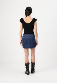 Svart volangtop, denim miniskjørt og høye svarte støvler med spenner. Antrekket har en tettsittende design med subtile teksturer.