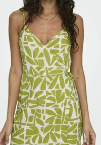 Robe blanche avec un motif de feuilles abstraites vertes, dotée d'un design portefeuille, d'une ceinture ajustable à la taille et de fines bretelles spaghetti.