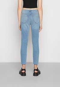 Jeans de ganga azul desbotados com um corte slim, bainha desfiada e dois bolsos traseiros. Estilizados com um top preto curto e sandálias pretas de sola grossa.