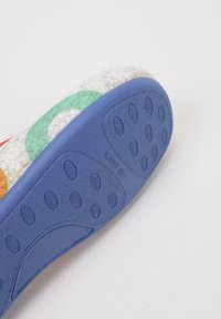 Suela de goma texturizada en azul con agarres de tracción circulares y etiqueta "SUELA DE GOMA"; la parte superior presenta diseños de fieltro coloridos en naranja, verde y amarillo.
