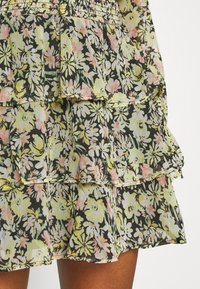 Gonna nera a balze con stampa floreale rosa, gialla e bianca indossata da una persona con pelle di tonalità marrone medio.