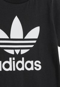 Schwarzer Stoff mit großem weißem Adidas-Trefoil-Logo und dem darunter gedruckten Wort "adidas" auf einem Kleidungsstück.