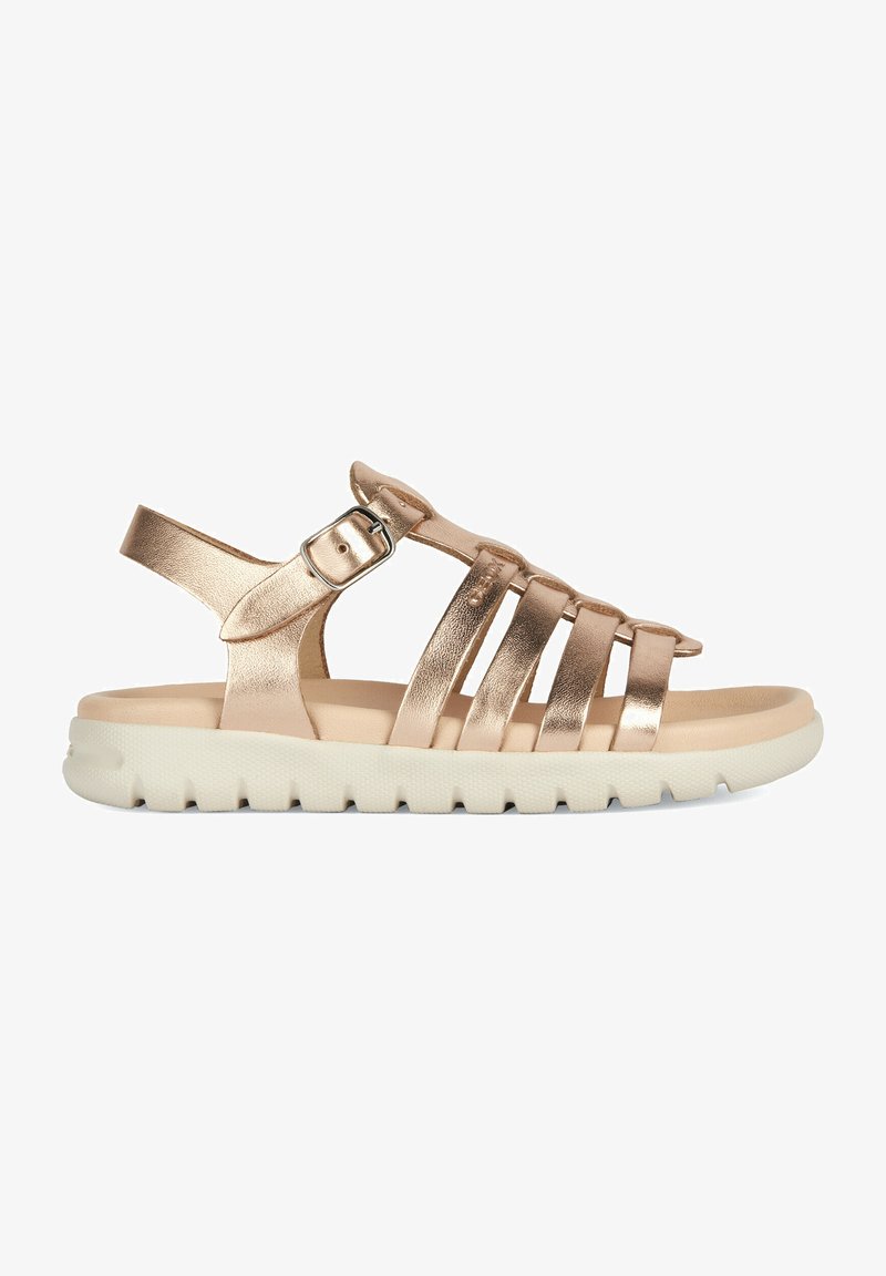 Metaliczne złote sandały z wieloma paskami, regulowanym zapięciem na kostkę, miękkim beżowym wkładem oraz teksturowaną białą gumową podeszwą.