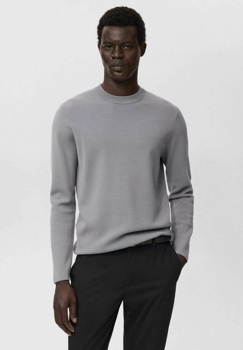 Hellgrauer Pullover aus weichem Strickstoff, mit Rundhalsausschnitt und langen Ärmeln, kombiniert mit schwarzen Hosen.