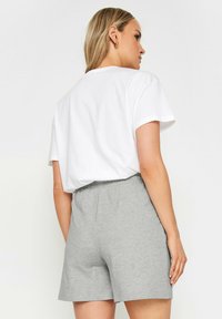 T-shirt en coton blanc à manches courtes, associé à un short gris élastique, de longueur mi-cuisse, avec une taille élastique.
