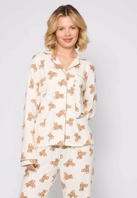 Pajama set made of soft, cream fabric featuring a repetitive bear pattern in brown. Includes a long-sleeve shirt and matching pants.