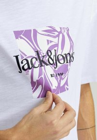Hvid bomulds T-shirt med et lilla grafisk design, der har blomster mønstre og sort tekst, der står "Jack & Jones" og "Est. 1990."