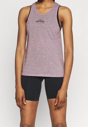 Woman wearing a sleeveless purple sports tank top with black shorts, standing against a white background.
