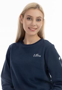 Felpa blu navy in morbido materiale con scollatura rotonda, caratterizzata da testo bianco e logo di un'ancora sul petto e un dettaglio con bottone sulla manica.
