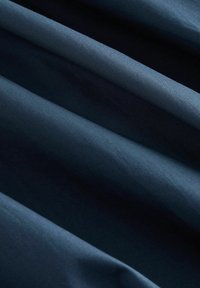 Tissu bleu foncé avec une texture lisse, présentant de douces plis et un éclat subtil. Le matériau semble léger et adaptable, adapté à diverses applications.