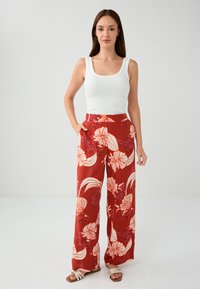 Rode wijde broek met witte bloemenpatronen, hoge taille, zijzakken, gecombineerd met een aansluitende witte tanktop en sandalen met bandjes.