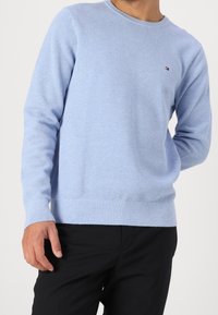 Hellblauer Strickpullover mit Rundhalsausschnitt, strukturiertem Muster sowie gerippten Bündchen und Saum. Mit kleinem Logo auf der Brust.