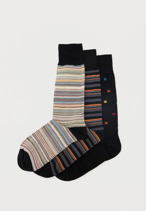 Trys blauzdinės ilgumo kojinės su juodomis rankovėmis ir kojų galais, baltame fone su įvairiais spalvotais dryžuotais ir kvadratų raštais.