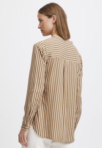 Brown and white striped long-sleeve shirt, featuring a back yoke, rounded hem, and buttoned cuffs. Smooth fabric with a relaxed fit.