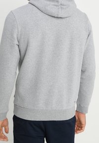 Sudadera gris con bolsillo canguro, cordón ajustable, puños y dobladillo de canalé. Fabricada con una suave y texturizada mezcla de algodón.