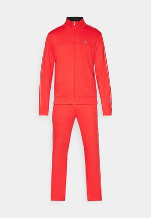 Punainen urheiluasu pehmeästä kankaasta. Vetoketjullinen takki, jossa on korkea kaulus ja sivuviivat. Yhteensopivat housut joustavalla vyötäröllä ja lahkeensuissa.