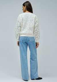 Sudadera de encaje floral blanco con cuello redondo, puños y dobladillo acanalados, combinada con jeans de mezclilla de pierna ancha en azul claro. Textura suave.