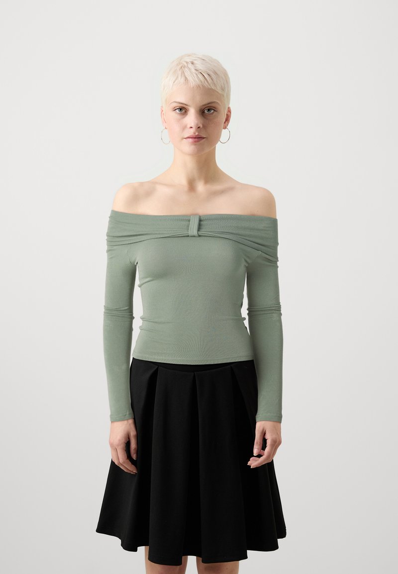 Off-the-shoulder, långärmad topp i mjuk grön tyg; åtsittande bodice med en frontknutdetalj. Matchad med en svart plisserad kjol.