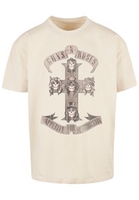 Beige cotton t-shirt featuring a graphic of a cross with five skulls, surrounded by 'Guns N' Roses' and 'Appetite for Destruction' banners.