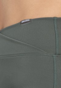 Leggings atletici verde scuro con una trama liscia, dotati di un'etichetta nella vita e di dettagli di cucitura sottili lungo i bordi esterni.