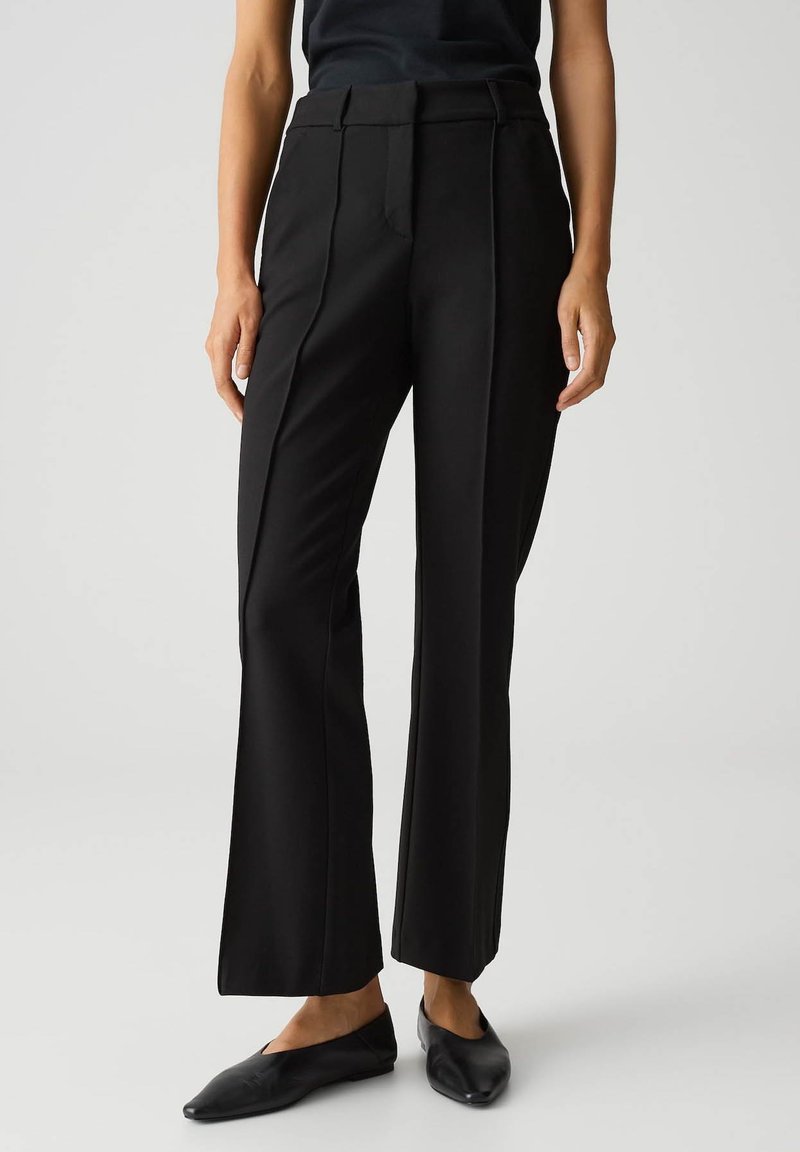 Zwarte op maat gemaakte broek met een geplooide pijp, vlakke voorkant en subtiele kreukdetails. Gemaakt van een soepele stof, te combineren met eenvoudige zwarte flats.