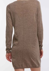 Robe pull en tricot marron avec des manches longues, un col rond et une finition texturée. Présente une couture arrière droite et un ourlet côtelé.