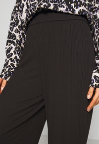Pantalon noir côtelé avec une taille haute, associé à un blouse à manches longues présentant un imprimé animal noir et violet.