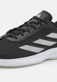 Black athletic shoe with a textile upper, silver striped accents, and a white outsole. Features round laces and a textured toe cap.