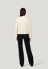Cremfarbener, kürzer geschnittener Pullover mit gerippten Bündchen, kombiniert mit schwarzen weiten Hosen. Strukturierter Strickstoff, minimalistisches Design.