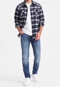 Koszula w kratę z długim rękawem w granatowo-białym kolorze, zestawiona z białym T-shirtem, niebieskimi dżinsami i białymi trampkami. Posiada kieszenie na piersi i luźny krój.