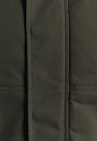 Tessuto verde scuro con una finitura testurizzata, caratterizzato da cuciture visibili e una superficie liscia. Il design è minimalista, senza motivi o accessori.