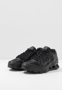 Black athletic shoes with a mesh upper, textured overlays, and a thick rubber sole. Features padded collar and lacing system for support.