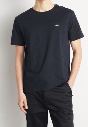 Dunkelblaue Baumwoll-T-Shirt mit kurzen Ärmeln und Rundhalsausschnitt. Verfügt über ein kleines gesticktes Logo auf der linken Brust. Glatte Textur.