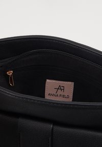 Wnętrze czarnej skórzanej torebki z kieszenią na zamek i metką. Gładka faktura, zaokrąglone krawędzie i złote elementy ozdobne na zamku.