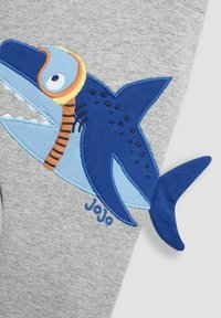 Grå leggings med et blåt hajdesign med en orange snorkel, broderede detaljer og en blå stofhaleaccent. "JoJo" tekst inkluderet.