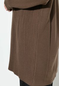 Brun virkad tröja med vertikal ribbad textur på sidorna, solid del på baksidan och en löst sittande passform.