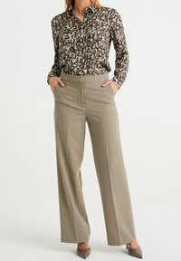 Blommönstrad skjorta med knappar i grönt och brunt, kombinerad med högmidjade, vida beige byxor med sidofickor och slät yta.