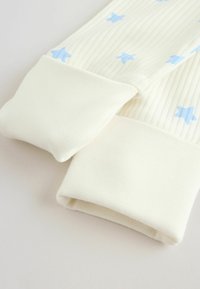 Približni prikaz kremasto obojenog tkanog materijala s plavim zvjezdicama i mekanim, presavijenim rubovima rukava dječje odjeće.