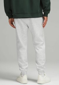 Lichtgrijze sweatpants met elastische boorden, gemaakt van zachte stof, gedragen met een donkergroen sweatshirt en witte sneakers. Geen zichtbare patronen of accenten.