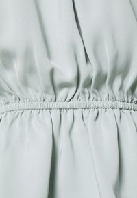 Tessuto verde menta chiaro con una consistenza morbida e liscia, caratterizzato da dettagli arricciati in vita per una vestibilità comoda.