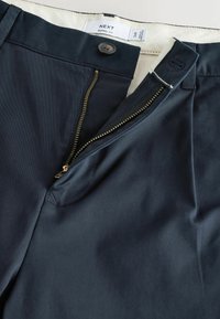Marineblaue Hose mit offenem Messingreißverschluss, Knopfverschluss und sichtbarem weißem Innenbund mit Aufschrift „NEXT Barrel Fit.“