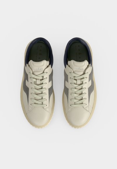 Ζευγάρι μπεζ και γκρι sneakers με κορδόνια και μαύρο εσωτερικό φόδρα, φωτογραφημένα από ψηλά σε απλό ανοιχτό φόντο.