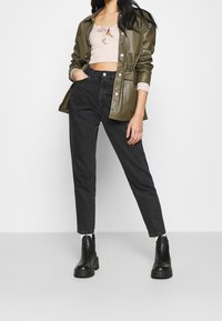 Veste-chemise en cuir vert, top court rose clair, jean noir taille haute et bottines noires à plateforme.