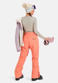 Roze sneeuwbroek met een ontspannen pasvorm, voorzien van een Roxy-logo, gecombineerd met een crèmekleurig langmouwtop en een gebreide muts met pompon.