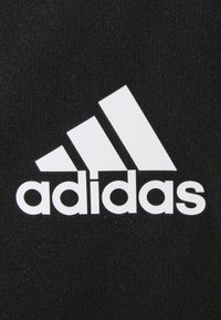 Bílé logo Adidas se třemi diagonálními pruhy a názvem značky na černém texturovaném pozadí.